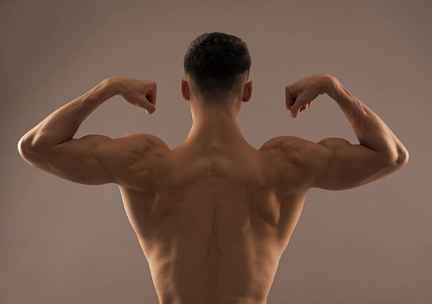 Ajuste hombre trasero torso flex brazo músculo mostrando bíceps tríceps fondo gris, flexión - Foto, imagen