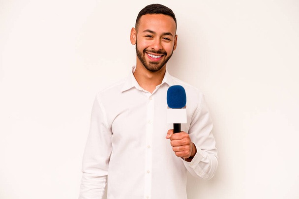 Junger hispanischer Fernsehmoderator isoliert auf blauem Hintergrund, lacht und hat Spaß. - Foto, Bild