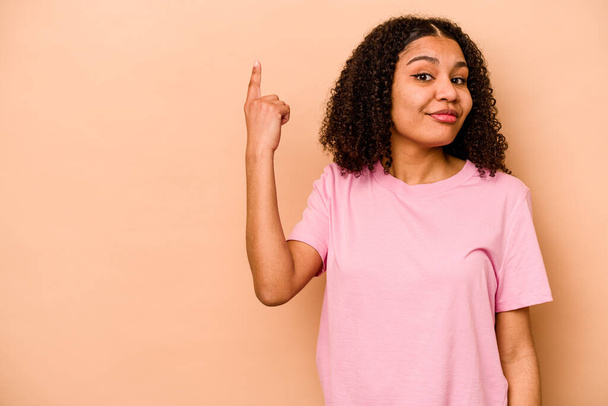 Νεαρή Αφροαμερικανή γυναίκα απομονωμένη σε μπεζ φόντο που δείχνει το νούμερο ένα με δάχτυλο. - Φωτογραφία, εικόνα