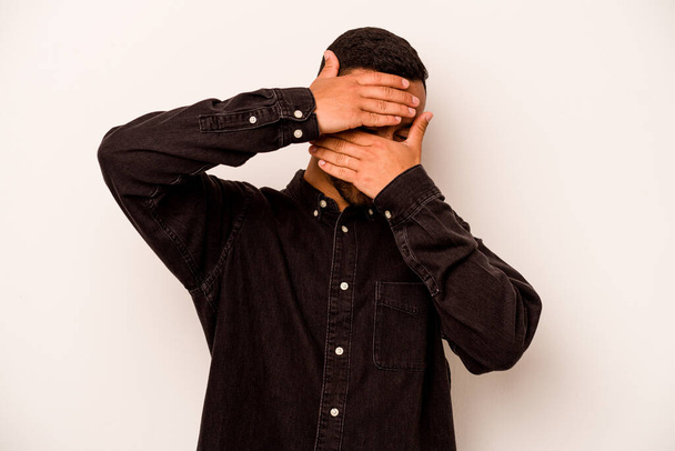 Young hispanic man isolated on white background blink at the camera through fingers, embarrassed covering face. - Φωτογραφία, εικόνα