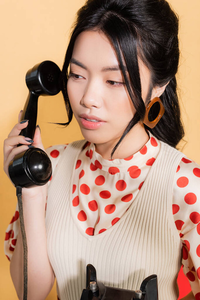 Portrait of asian model holding retro telephone on orange background - Foto, Imagen