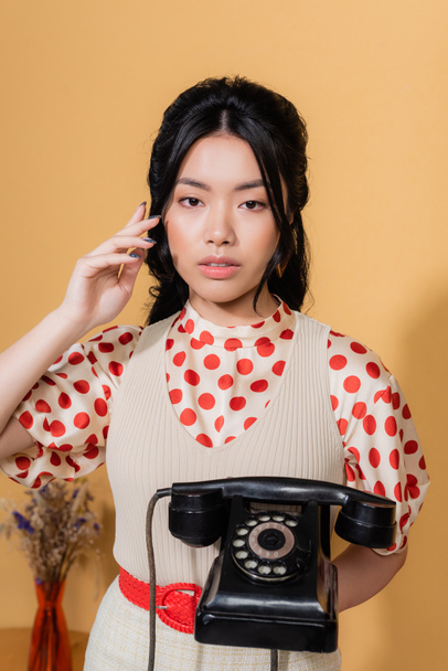 Asian model holding vintage telephone and looking at camera on orange background - 写真・画像