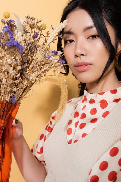 Portrait of stylish asian model holding vase with flowers on orange background - Foto, immagini