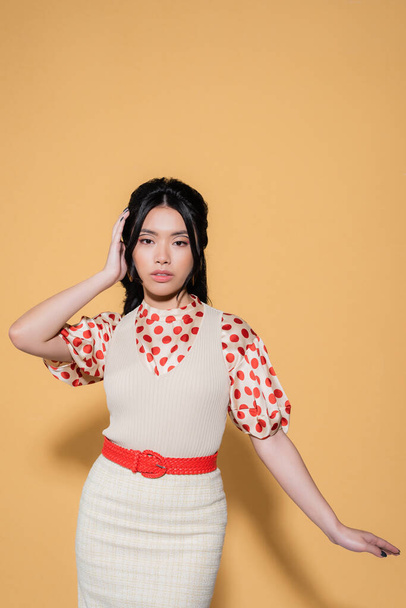 modèle asiatique à la mode en chemisier et robe en regardant la caméra sur fond orange - Photo, image
