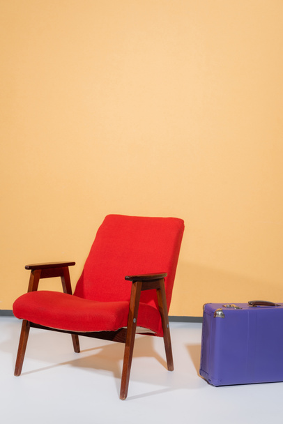 Vintage Sessel in der Nähe Koffer auf orangefarbenem Hintergrund - Foto, Bild