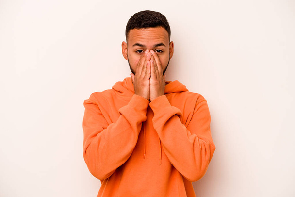 Young hispanic man isolated on white background covering mouth with hands looking worried. - 写真・画像
