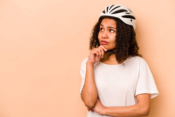 Giovane donna ispanica indossa un casco bici isolato su sfondo blu guardando lateralmente con espressione dubbia e scettica. - Foto, immagini