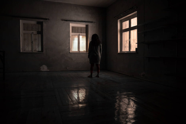 Τρομακτική σιλουέτα μέσα σε εγκαταλελειμμένο ανατριχιαστικό δωμάτιο με παράθυρο τη νύχτα. Τρομακτική σκηνή. Απόκριες. - Φωτογραφία, εικόνα