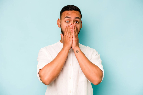 Young hispanic man isolated on blue background shocked covering mouth with hands. - Foto, immagini