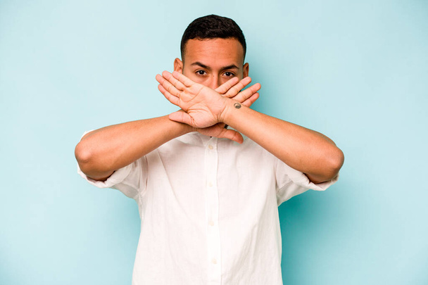 Junger hispanischer Mann isoliert auf blauem Hintergrund und macht eine Dementi-Geste - Foto, Bild