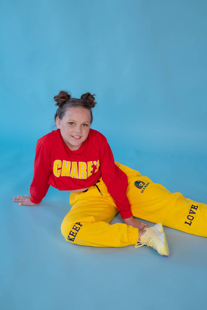 tiener meisje in de mode stijlvolle heldere kleren. kleine dame in rood en geel op blauwe achtergrond. make-up en kapsel. - Foto, afbeelding