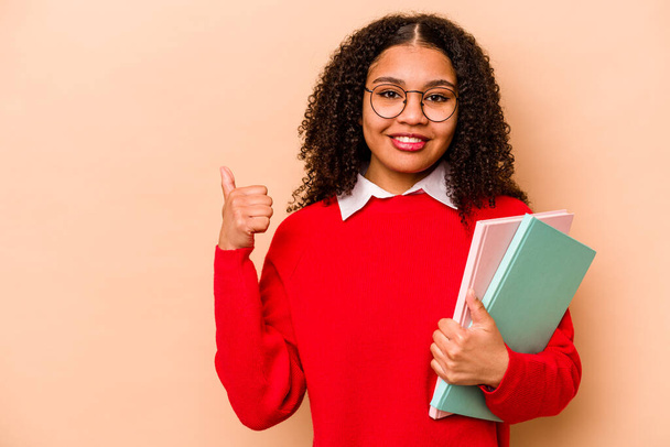 Young student African American woman isolated on beige background smiling and raising thumb up - Φωτογραφία, εικόνα