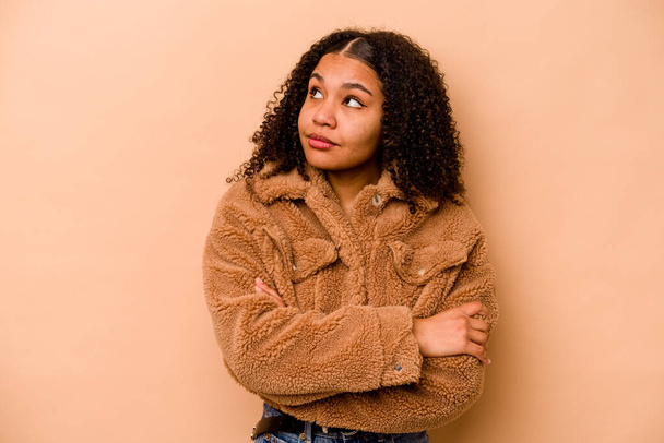 Joven mujer afroamericana aislada sobre fondo beige soñando con lograr metas y propósitos - Foto, Imagen