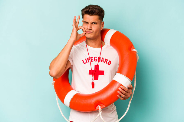 Young caucasian lifeguard isolated on blue background with fingers on lips keeping a secret. - Photo, Image