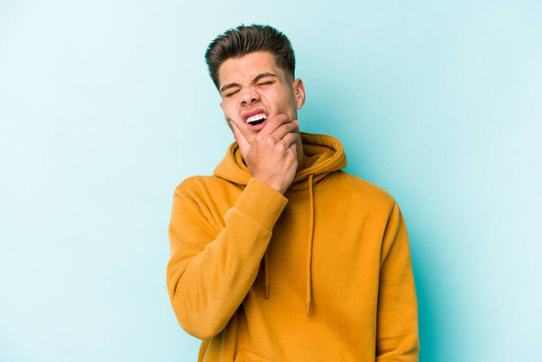 Jonge blanke man geïsoleerd op blauwe achtergrond met een sterke tanden pijn, molaire pijn. - Foto, afbeelding