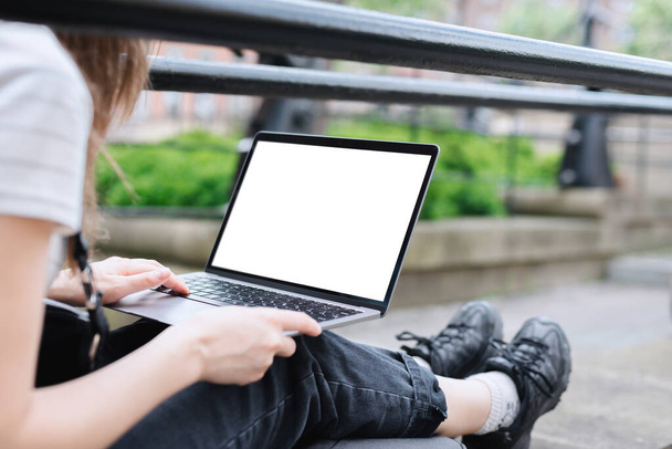 Dziewczyna pracuje w laptopie, siedzi na kamiennym parapecie w parku. Dziewczyna pracuje na dworze..  - Zdjęcie, obraz