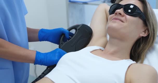Woman client in protective glasses having laser hair removal of armpit in beauty salon 4k movie - Imágenes, Vídeo