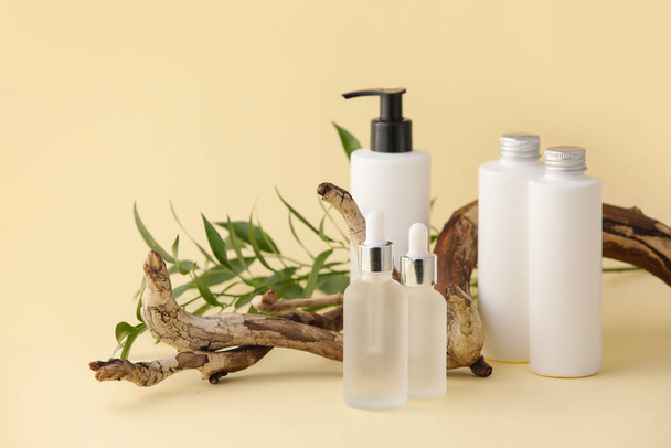 Bottles of natural serum, tree branch and plant leaves on yellow background - Foto, imagen