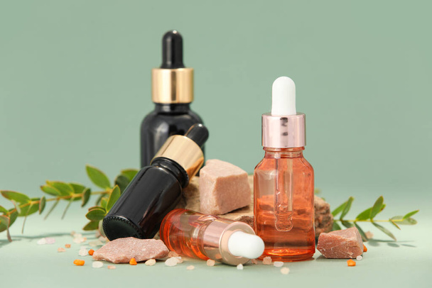 Bottles of natural serum, salt and plant leaves on green background - Photo, Image