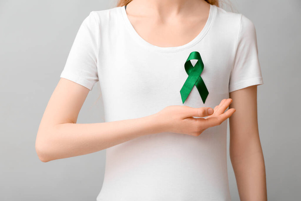 Woman in white t-shirt with green ribbon on grey background. Liver cancer concept - Foto, Imagem