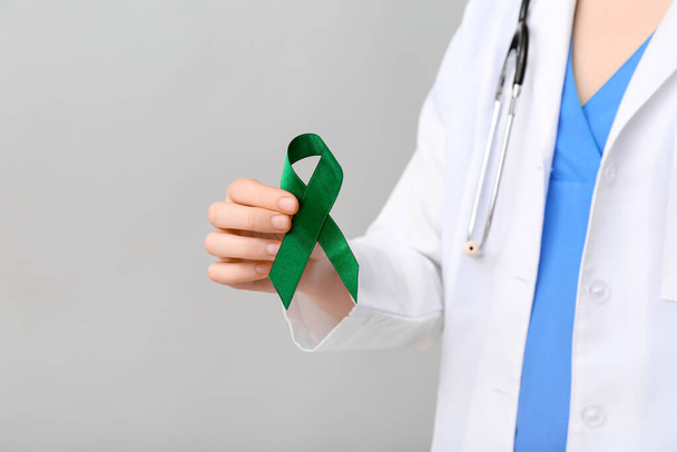 Vrouwelijke arts met groen lint op grijze achtergrond, close-up. Begrip leverkanker - Foto, afbeelding