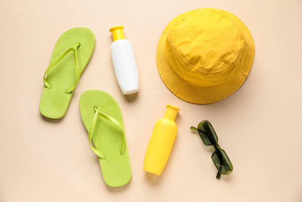 Botellas de protector solar con chanclas, gafas de sol y sombrero sobre fondo beige - Foto, imagen
