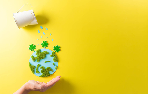 Hands holding paper earth with tree on yellow background. World environment day, earth day and save earth concept. - Photo, Image
