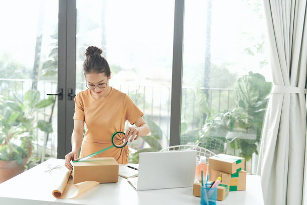 Startup malé firmy majitel pracuje doma, ženy těsnění lepenkové krabice s lepicí páskou, - Fotografie, Obrázek