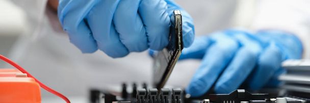 Un hombre en producción inserta un microcircuito en un dispositivo - Foto, Imagen