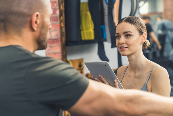 Beautiful Caucasian woman writes down a workout plan with a trainer at the gym - Photo, Image