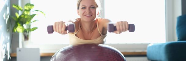 Woman doing exercises with dumbbells on a sports ball - Photo, image