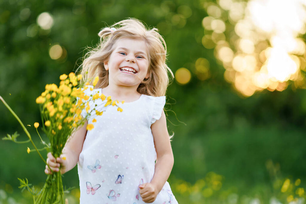 Adorável bonito menina pré-escolar em uma flor de dente de leão na natureza no verão. Criança bonita saudável feliz com flores, se divertindo. Luz brilhante do pôr-do-sol, miúdo activo. - Foto, Imagem