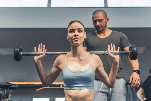 Portrait en salle de gym d'une brune confiante concentrée dans un soutien-gorge de sport gris à l'aide d'une haltère et profiter de son temps à la salle de gym. - Photo, image