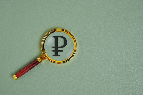 Ruble symbol under magnifying glass, on green background - Foto, imagen