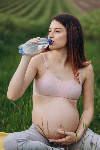 Pregnant woman drinking water after fitness. Thirsty after training expectant lady close-up, free space, sun light flare - Valokuva, kuva
