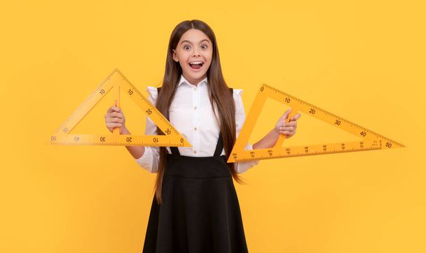 erstaunt Teenie-Mädchen in Schuluniform halten Mathematik-Dreieck zum Messen, Wissen - Foto, Bild