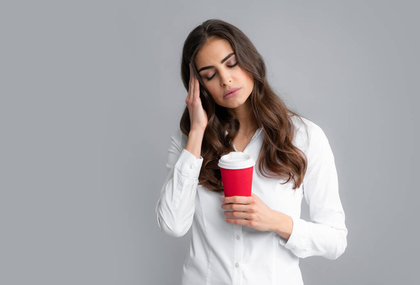 Portrait of a tired sleepy curly brunette woman holding takeaway coffee cup isolated over gray background. - Foto, Imagen