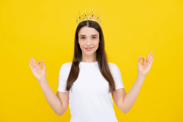 Portrait of arrogance woman with golden crown on head, leadership and success. Attractive rich arrogant girl wearing crown isolated over yellow background. - Фото, изображение
