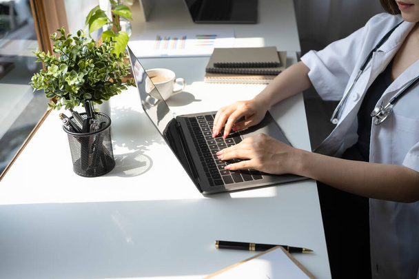 Žena lékař v bílé uniformě pracuje s notebookem a dokumenty v lékařské ordinaci. - Fotografie, Obrázek