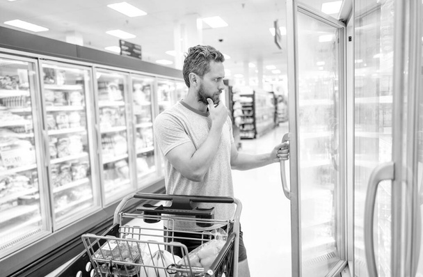 pondering man with shopping cart buying food at grocery, hypermarket - Foto, Imagem