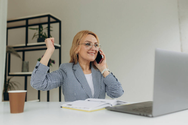 Beautiful middle age woman working at the office drinking a cup of coffee very happy and excited doing winner gesture with arms raised, smiling and screaming for success. celebration concept - Фото, изображение