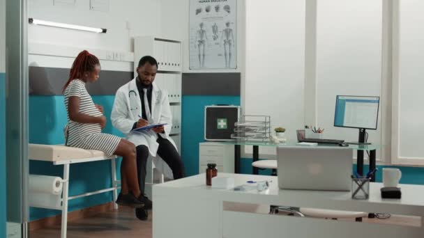 Médico do sexo masculino tomando notas na visita de check-up com a mulher grávida - Filmagem, Vídeo