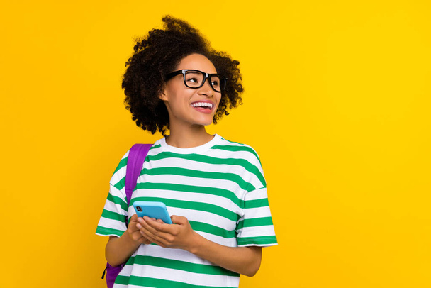 Photo of impressed young brunette lady look promo hold telephone wear eyewear t-shirt bag isolated on yellow background - Φωτογραφία, εικόνα
