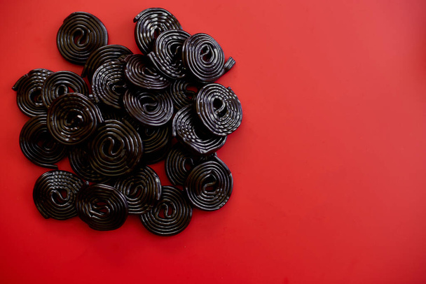 Flat lay smakelijke zwarte drop snoepjes op rode achtergrond, Snoep smaak zoethout, bovenaanzicht. - Foto, afbeelding