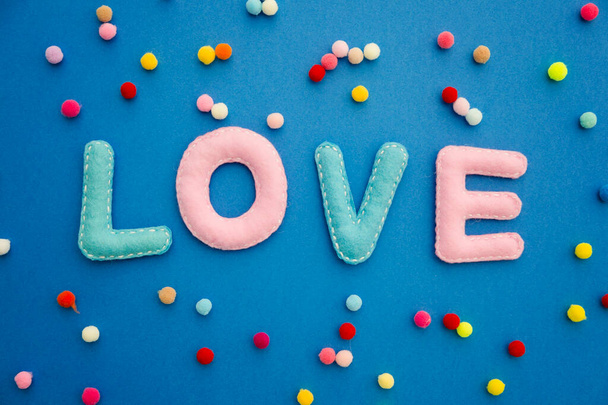Gefüllte Filzbuchstaben auf Hintergrund. Das Wort "Liebe" ist mit Bommelmützen verziert. Valentinstag-Thema. Grußkarte für Verliebte. Geschenkkarte mit Gefühlen. Handgemachte Kunst. - Foto, Bild