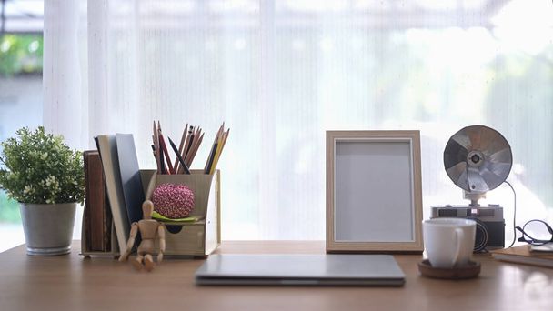 Scrivania home office con computer portatile, pianta in vaso, fotocamera retrò e tazza di caffè. - Foto, immagini