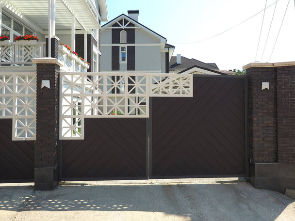 Een bruin-wit patroon hek omringt een huis in Europese stijl op een zonnige dag - Foto, afbeelding