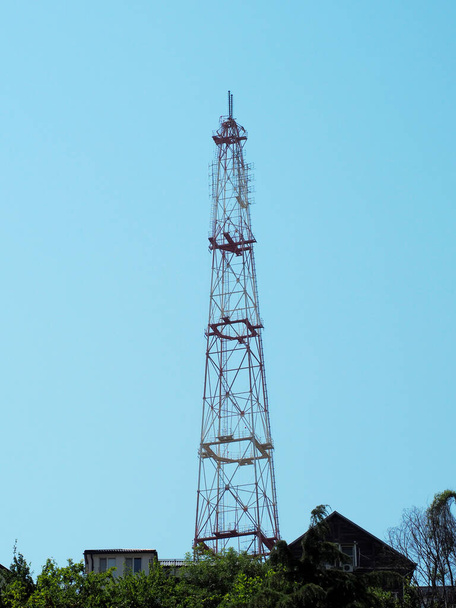 Egy magas mobiltorony emelkedik a háztetők fölé a kék égbolttal szemben. - Fotó, kép