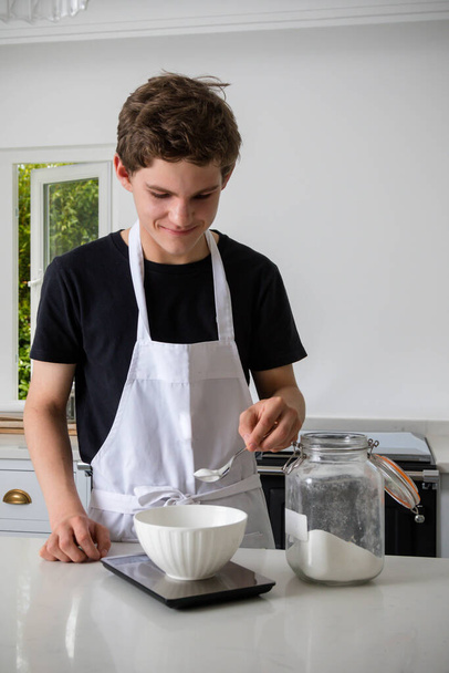 A teenage boy in a domestic kitchen weighing ingredients - Foto, Imagen