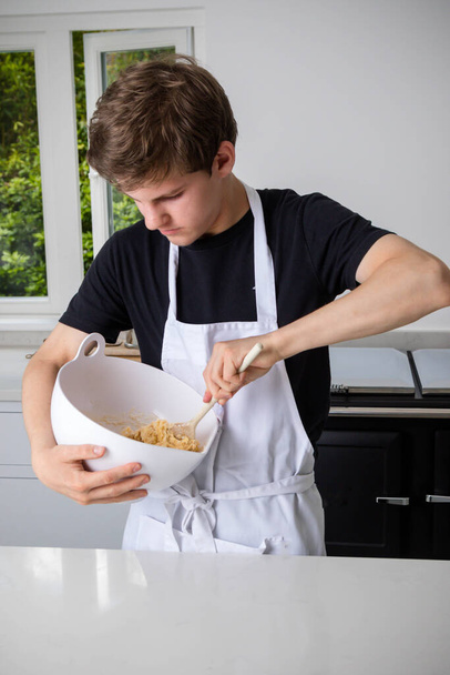 A teenage boy in a domestic kitchen hand mixing  - Photo, image